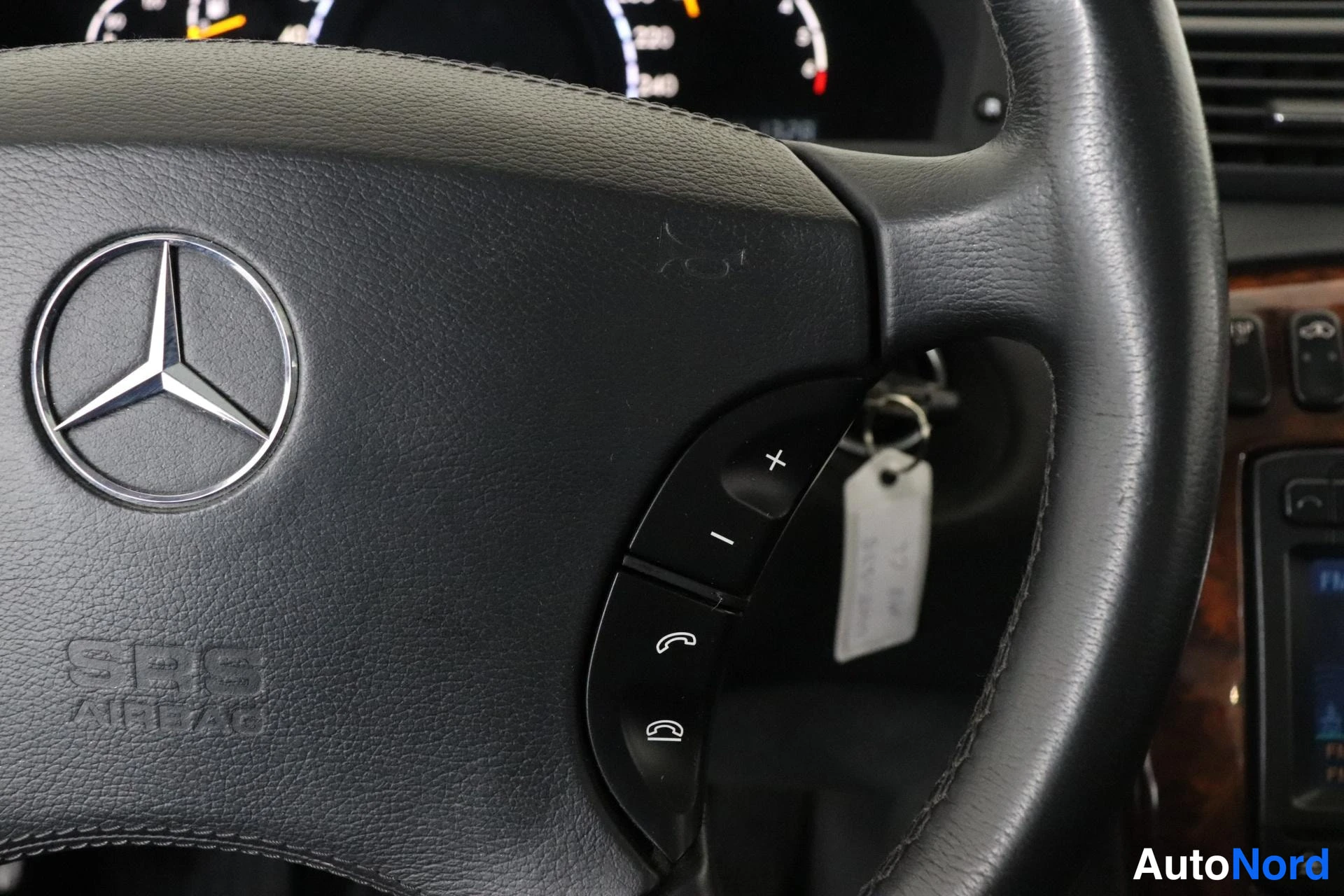 Edestä: Sisäkuva: Mercedes-ohjauspyörä tähtimerkällä, SRS AIRBAG -tekstillä ja puhelinpainikkeilla, avain virtalukossa tunnistelapulla ja kojelauta taustalla.