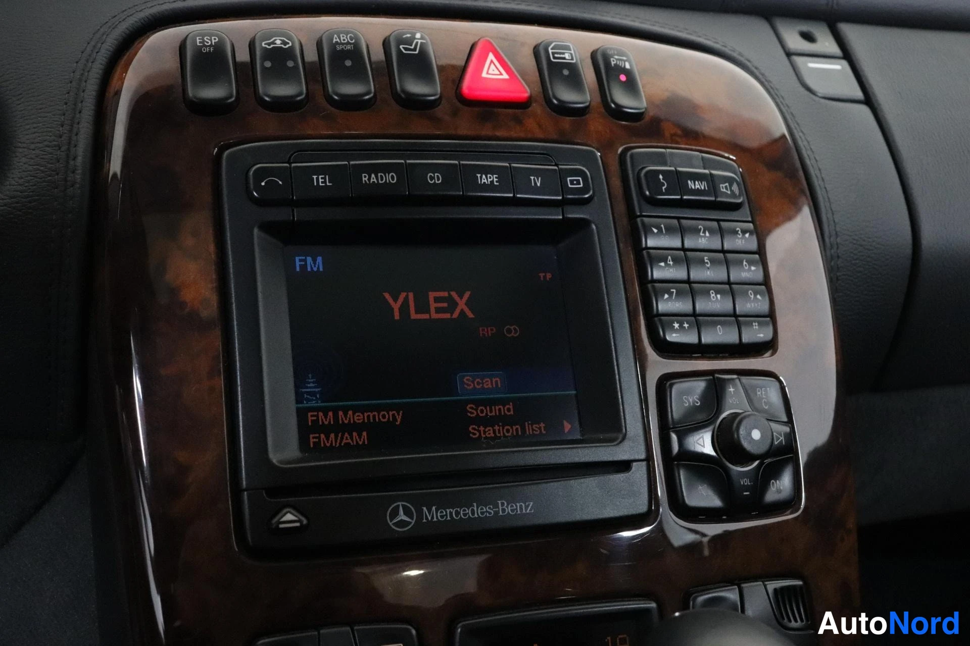 Ohjaamo: Close-up of the dashboard showing navigation system, radio and buttons including 'ABC Sport' on wood grain trim.