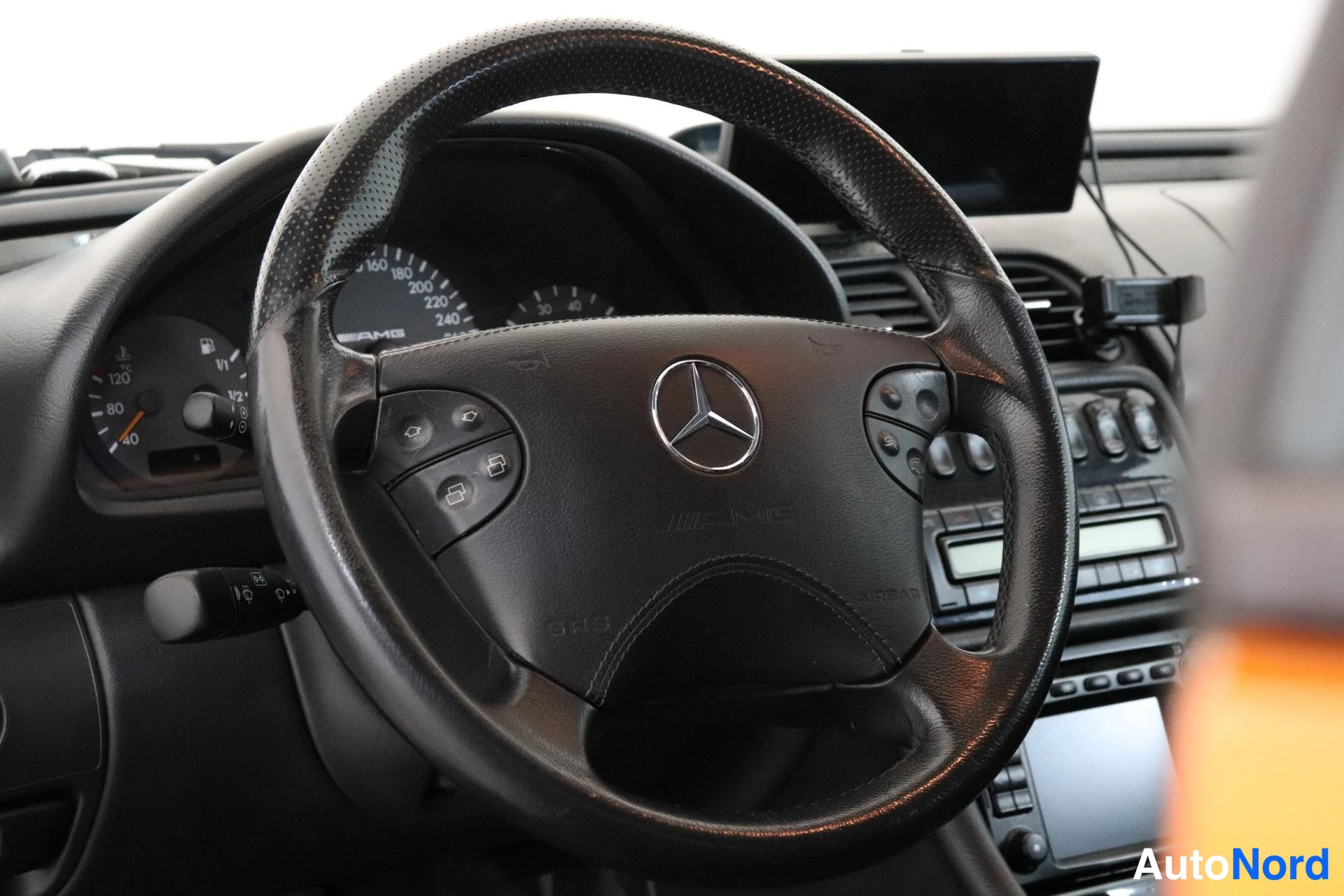 Sivulta: Ohjaamo sisältä: musta Mercedes-AMG-ohjauspyörä monitoimipainikkeilla, mittaristo ja kojelautaan kiinnitetty näyttö.