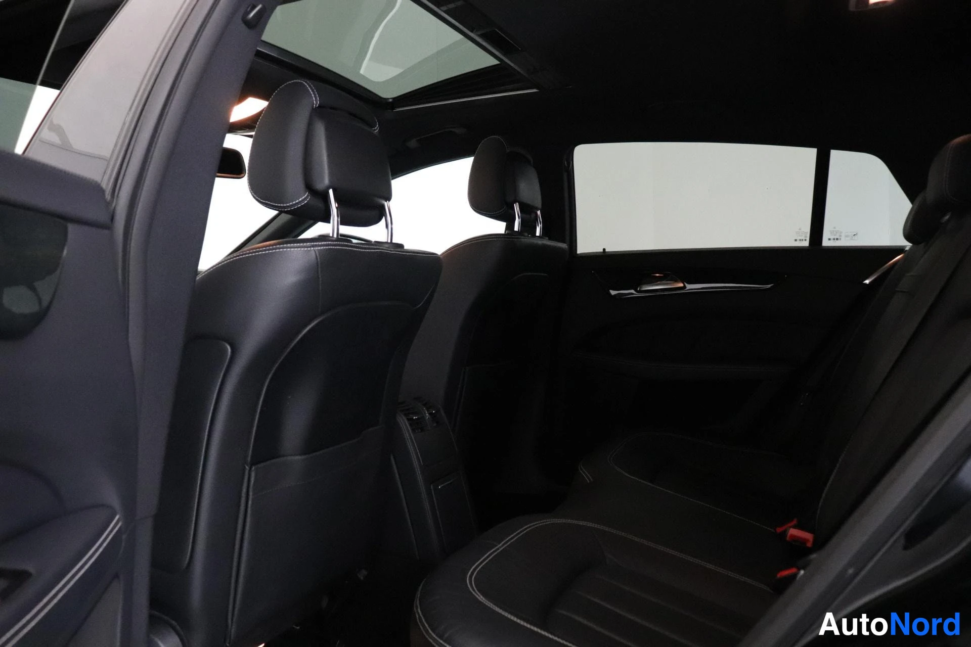 Takaistuimet: Interior view of the back seat area showing two black leather rear headrests and a panoramic glass sunroof above the cabin roof line.
