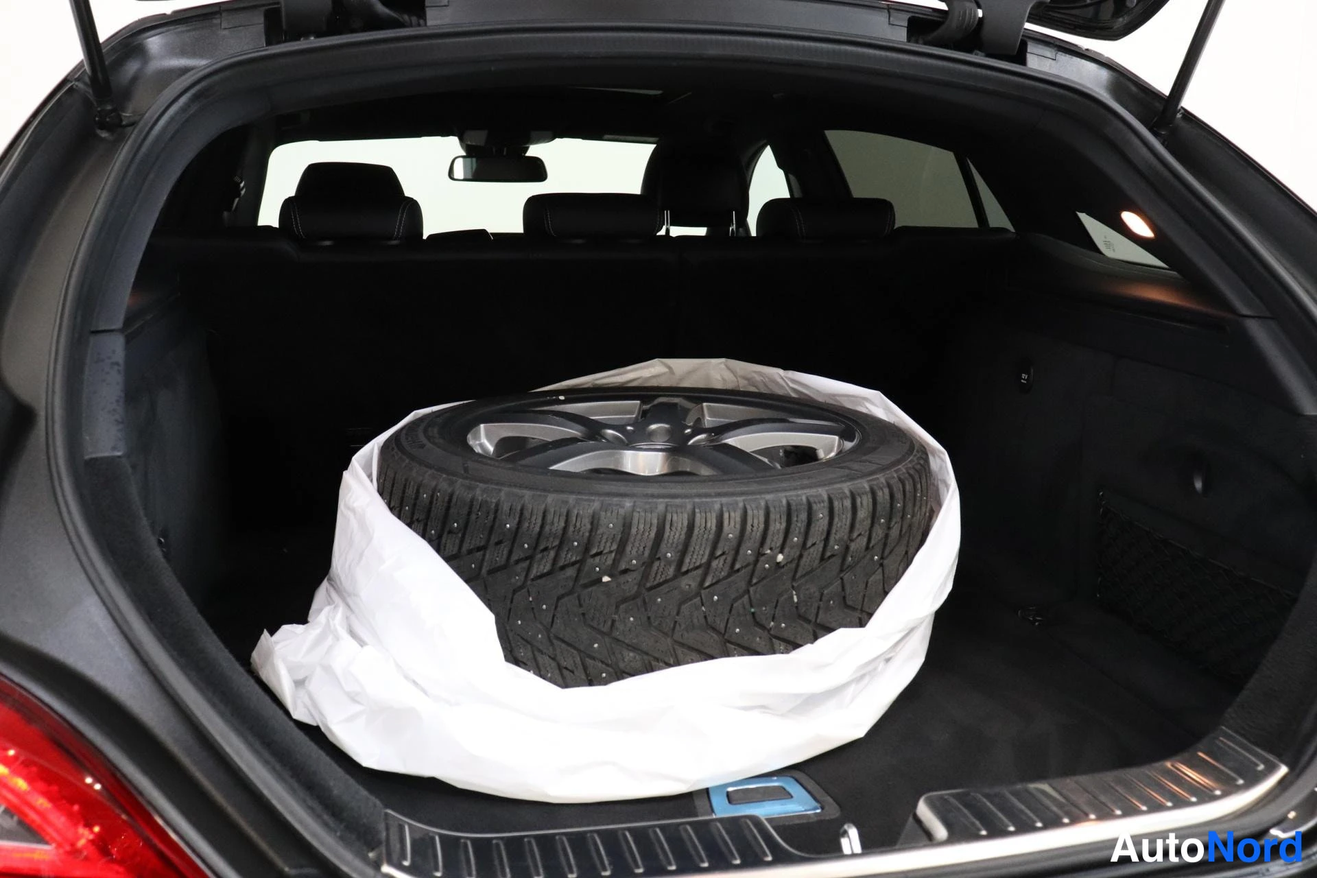 Tavaratila: Open trunk boot interior featuring a space-saver spare wheel in white protective wrapping. The alloy rim has a dark metallic finish with a central logo cap. Met