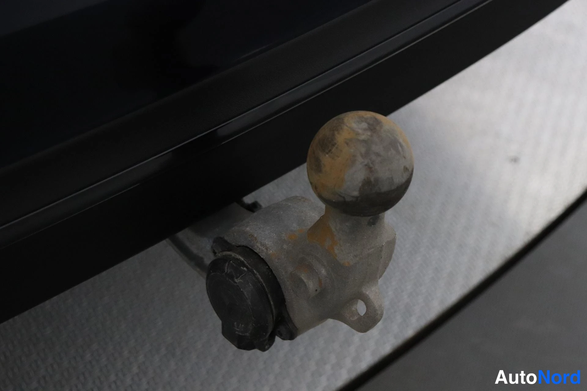 Yksityiskohta: Lähikuva vetokoukusta, joka on kiinnitetty autoon. Vetokoukku on metallinen ja sen yläpuolella on musta kansi. Vetokoukun alla on metallinen putki, joka on kiin