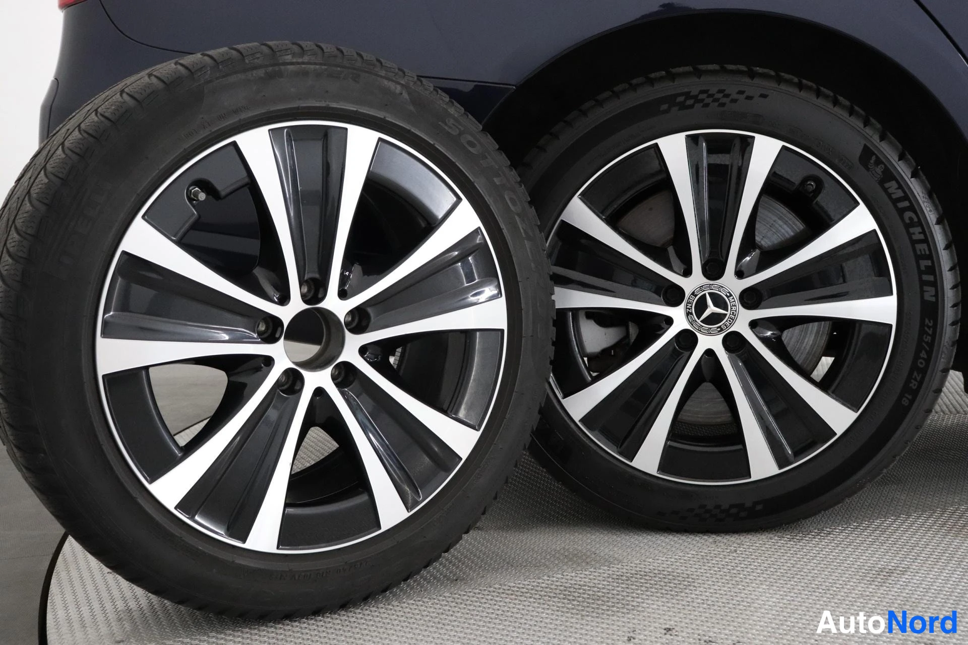 Yksityiskohta: Lähikuva kahdesta renkaasta, joissa on Mercedes-Benzin logo. Renkaat ovat Michelin-merkkisiä ja niissä on hopeanruskeita ja mustia jousirinteitä. Rengaskaaret o