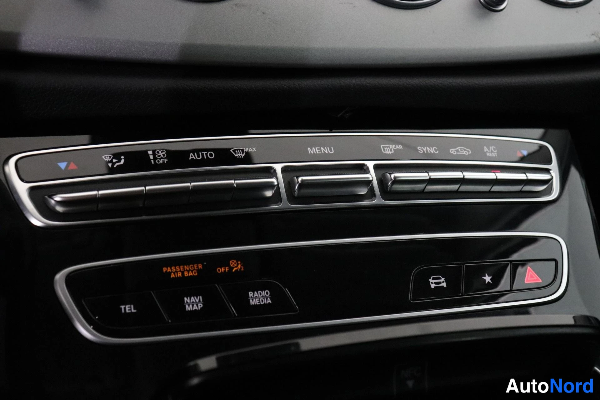 Muu: Keskiroodin ilmastointi- ja mediapaneeli lähikuvassa: AUTO-, MENU-, SYNC- ja A/C-painikkeet, TEL-, NAVI MAP- ja RADIO MEDIA -painikkeet, oranssina palava PASSEN