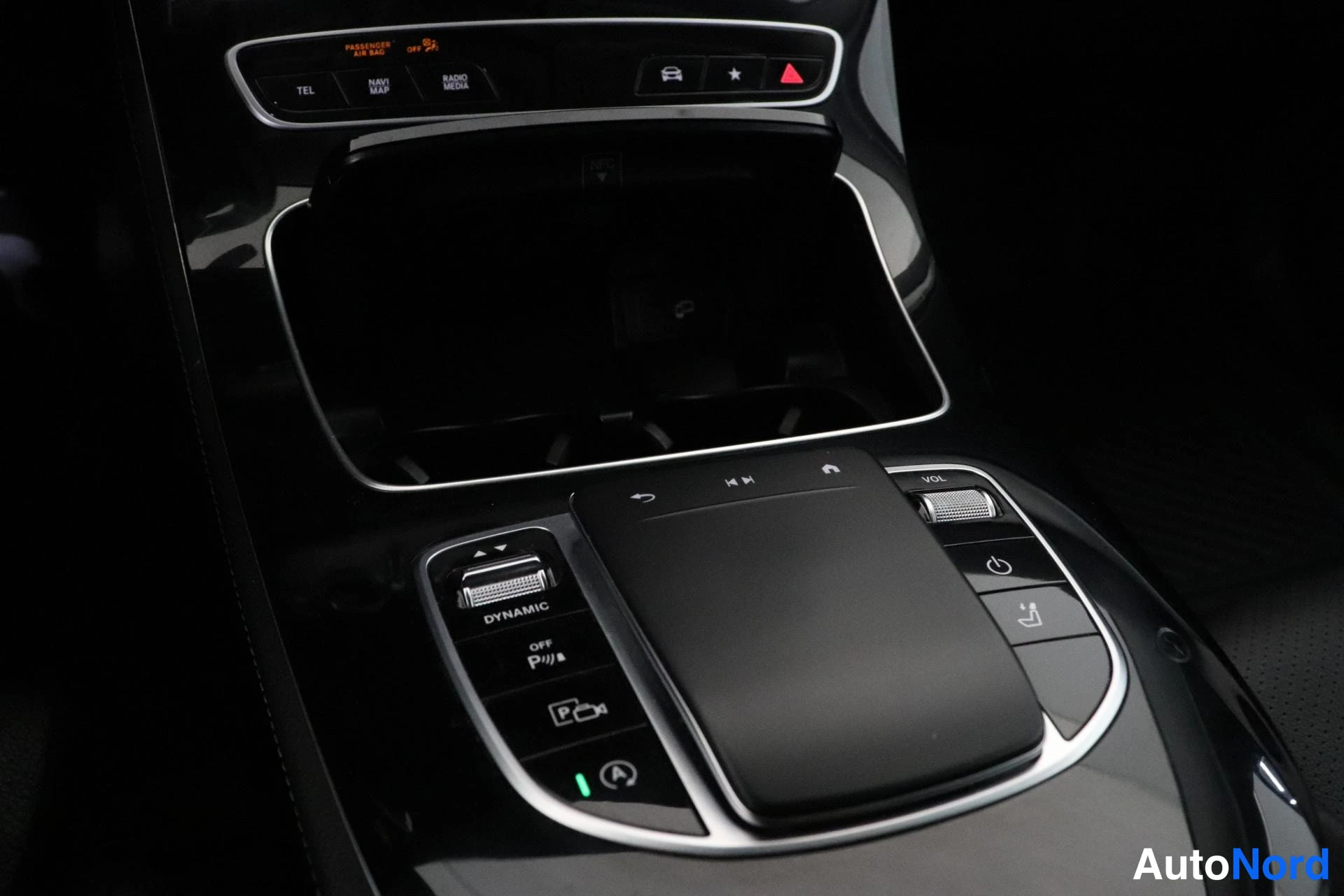 Yksityiskohta: Close-up of the car centre console showing the touchpad control, silver trim ring, DYNAMIC mode button, parking sensor switch and climate control switches.