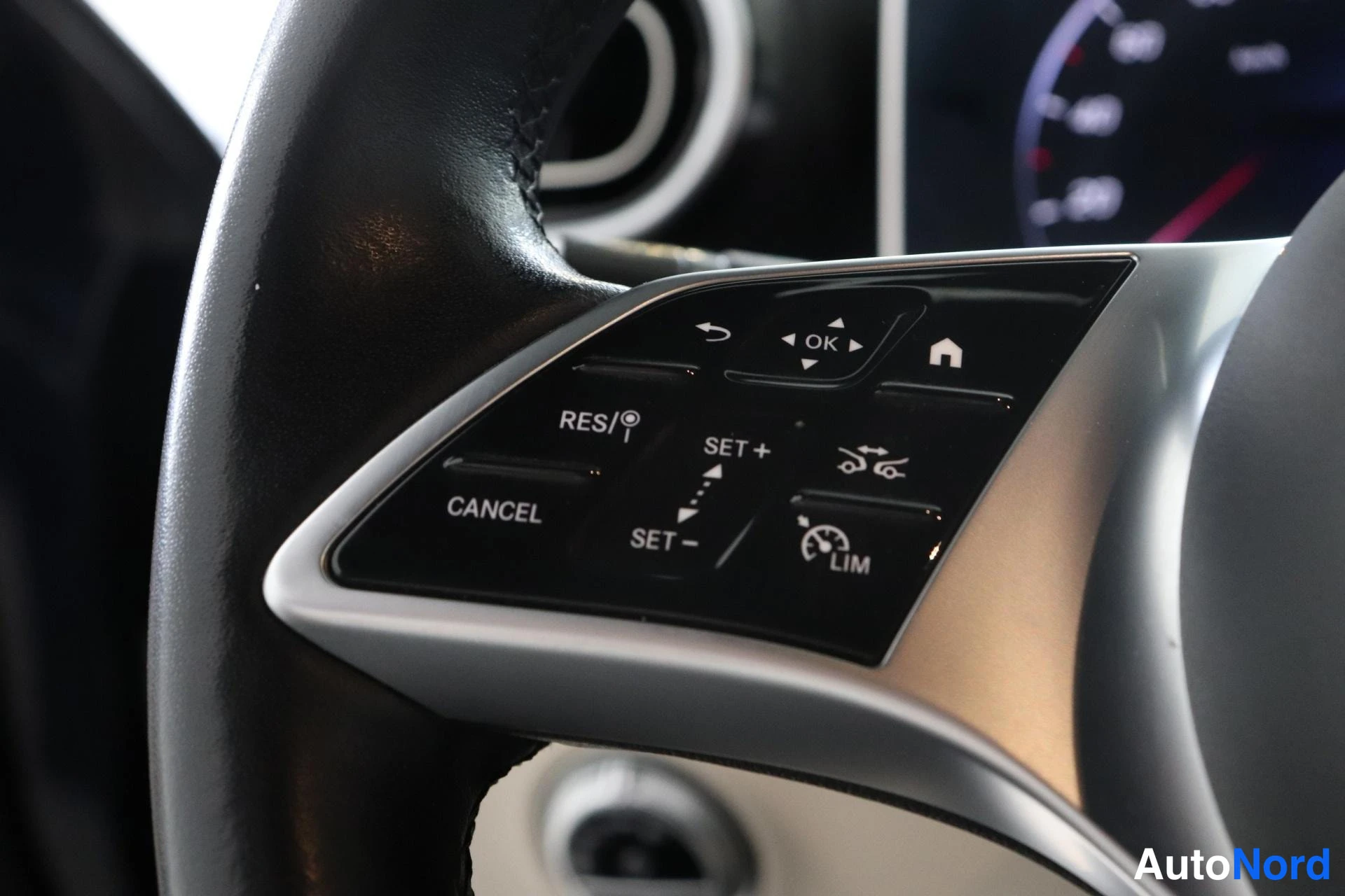 Yksityiskohta: Close-up of the left spoke on a multifunction steering wheel, showing buttons for cruise control (RES, SET+, SET-, CANCEL) and driver assistance features like a