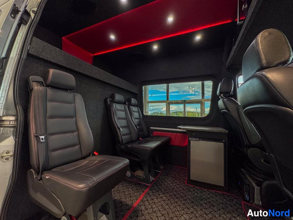 Ohjaamo: The interior of a custom van showing black leather seats arranged in rows. The ceiling has red ambient lighting strips and small spotlights. A side window is vi