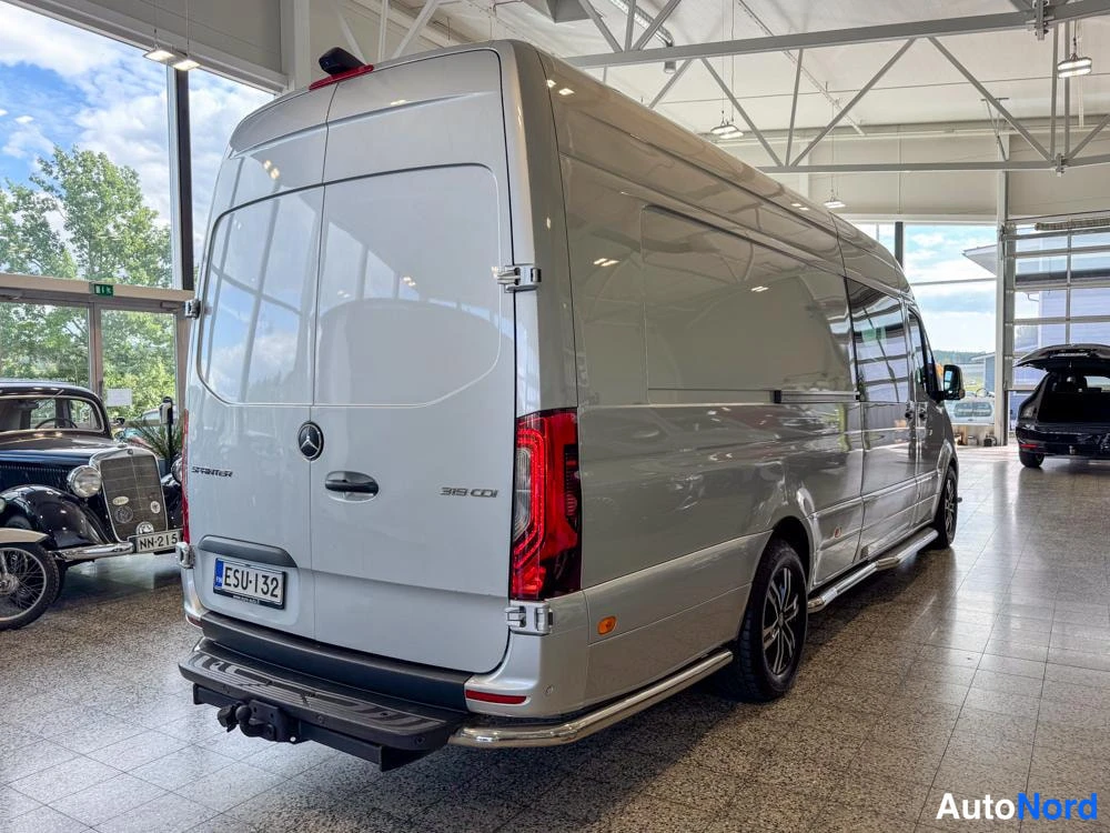 Takaviisto: Takaoikea näkymä autotallista hopeanvärisestä Mercedes-Benz Sprinter -pakettiautosta. Takapää, oikea puoli, takavalo, tavaratilaa peittävät metalliset oviruuvit