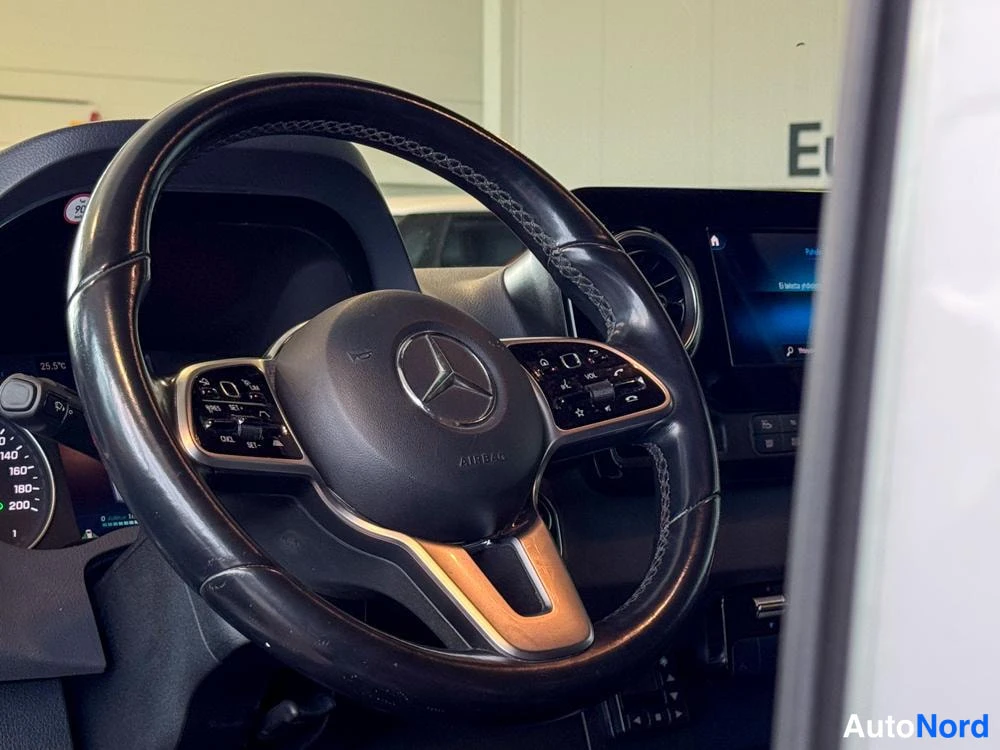 Sivulta: Mercedes-ohjauspyörän lähikuva: tähtimerkki, AIRBAG-teksti, monitoimipainikkeet ja näkyvissä osa digitaalisesta mittaristosta sekä keskinäytöstä.