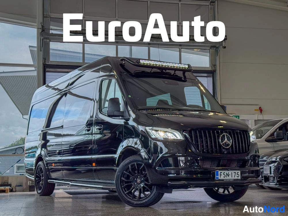 Etuviisto, nokka oikealle: Musta Mercedes-Benz Sprinter -pakettiauto etukulmasta sisätiloissa, nokka oikealla; katolla pitkä LED-valopalkki, mustat vanteet ja rekisteri.