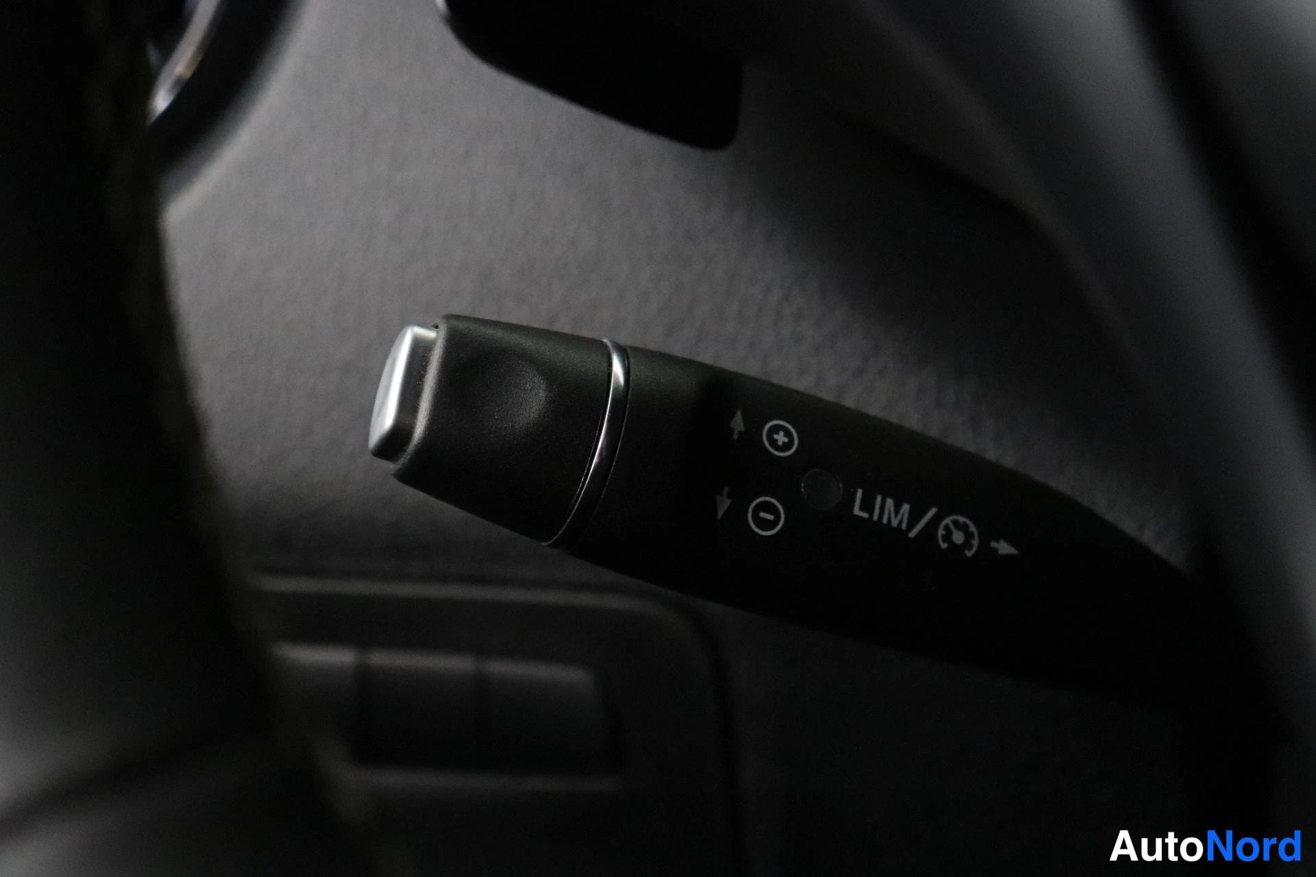 Yksityiskohta: Detail of a black control stalk behind the steering wheel showing markings for cruise control functions labeled LIM.