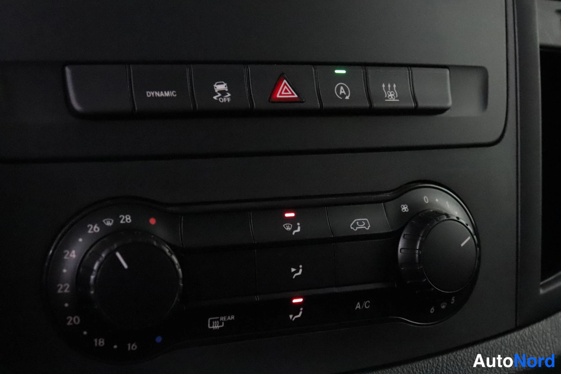 Yksityiskohta: Lower section of the center console showing climate controls with two rotary dials for temperature and buttons for fan settings.