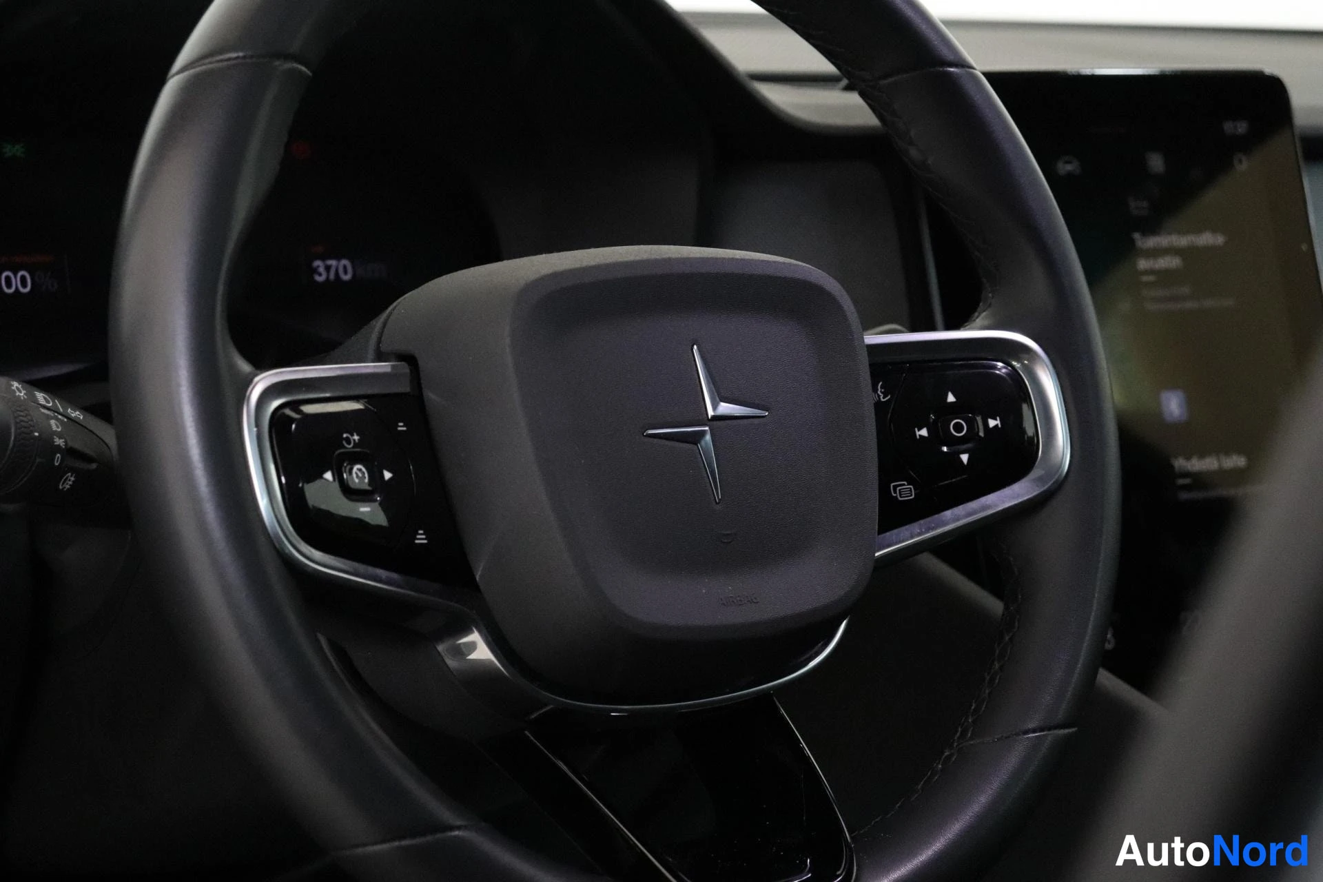 Muu: Ohjauspyörän lähikuva, napan keskellä Polestar-tähtilogo. Taustalla näkyy osittain digitaalinen mittaristo, jonka lukemana 370 km, sekä keskikonsolin kosketusnä