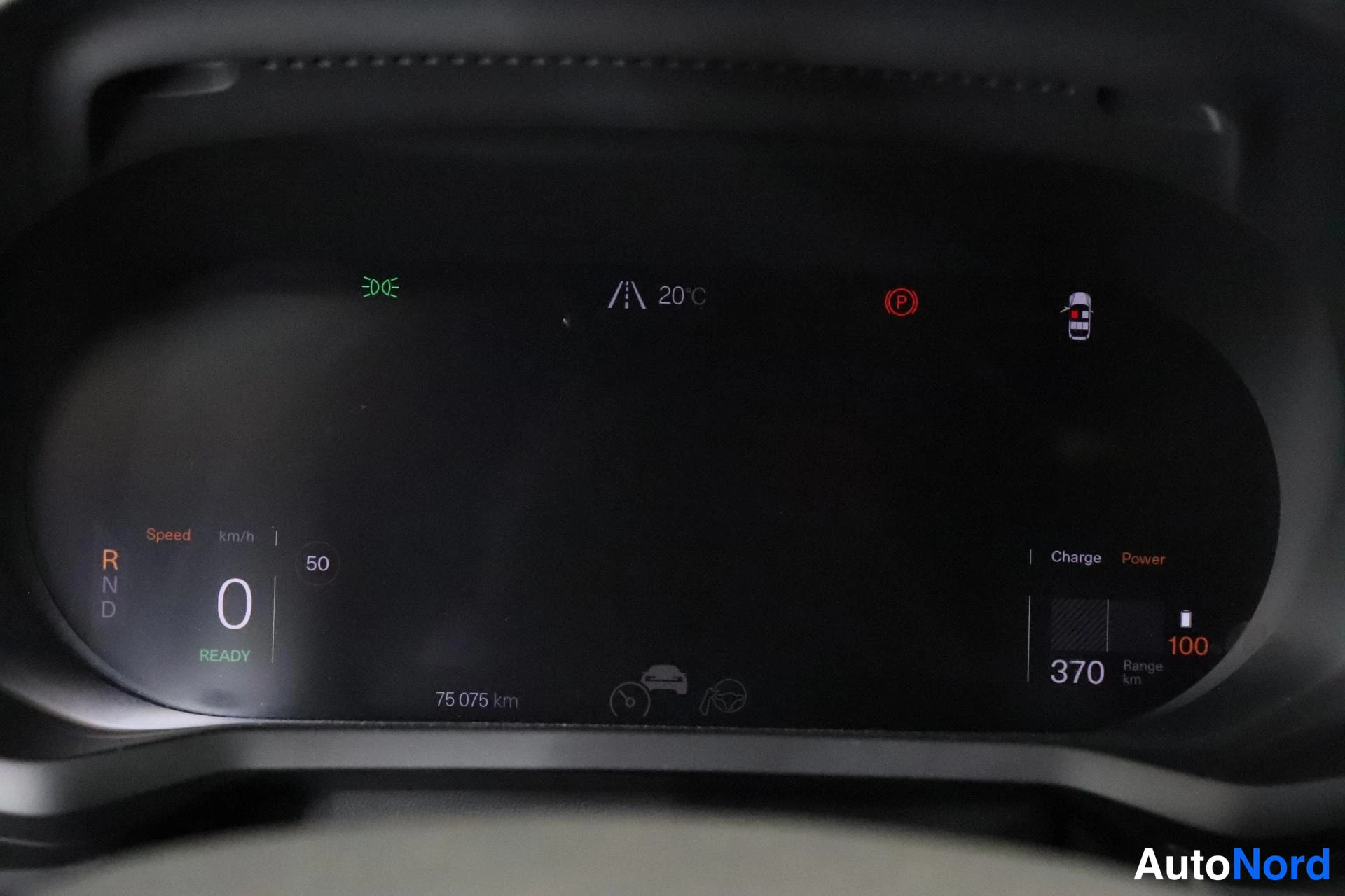 Yksityiskohta: Sähköauton digitaalinen kojelauta näyttää valmiustilassa (READY): nopeus 0 km/h, vaihdevalinta R/N/D R valittuna, matkamittari 75 075 km, toimintasäde 370 km, l