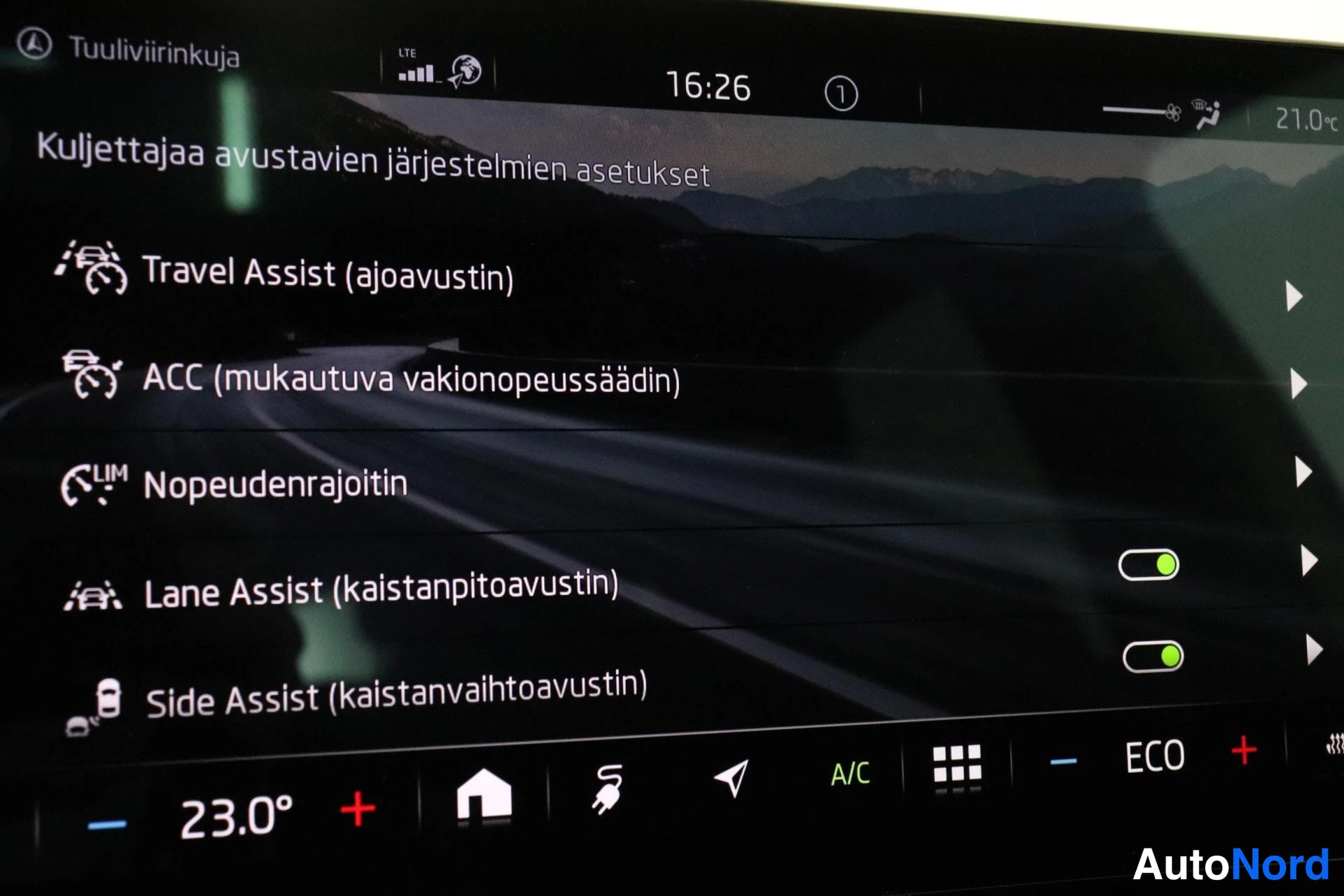 Ohjaamo: Infotainment screen showing driver assistance settings list. Time 16:26 shown at top; 'Lane Assist (kaistanpitoavustin)' and 'Side Assist (kaistanyhtyavustin)'
