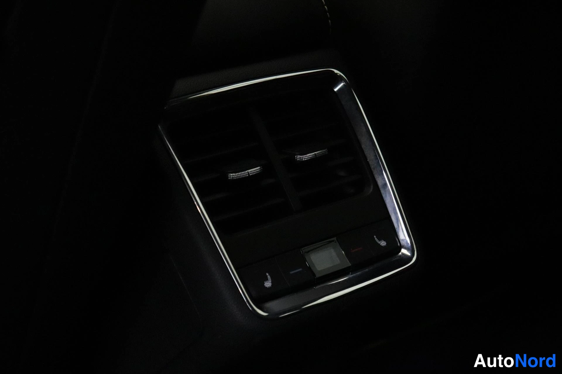 Yksityiskohta: Close-up of rear center air vent with two illuminated heating icon buttons (seated figure symbol) lit on the trim bezel below vents.