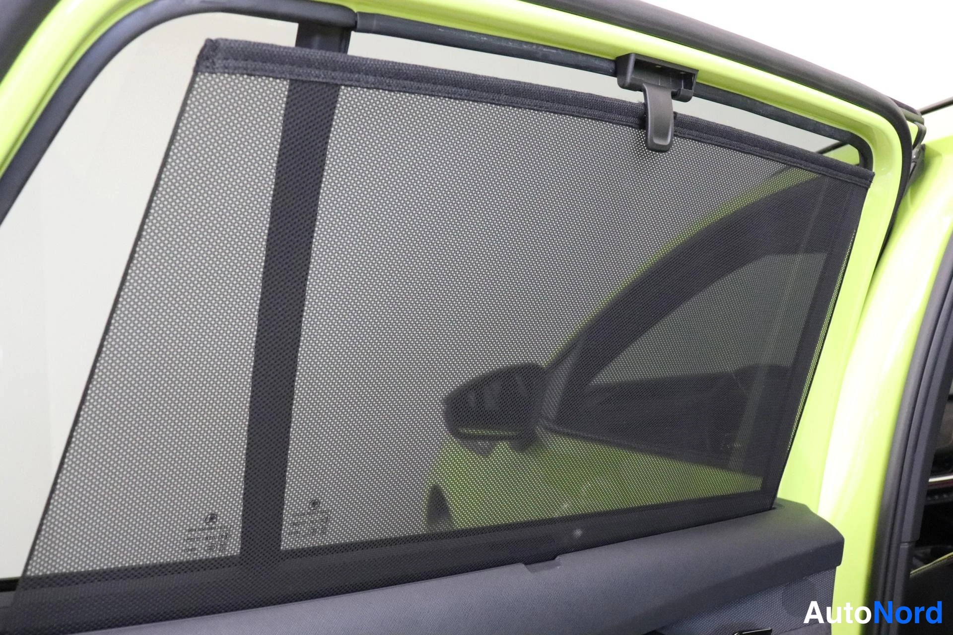 Yksityiskohta: Avoimen oven lasin takana musta verkkoaurinkosuoja; kori kirkkaan keltavihreä.