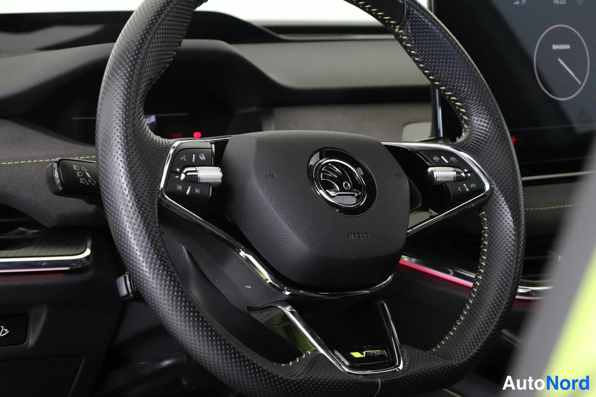 Edestä: Auton sisätilat: Skoda-ohjauspyörä lähikuvassa, jossa keskellä Skodan logo ja alaosassa VRS-merkki. Ohjauspyörässä monitoimipainikkeet molemmin puolin ja vihreä