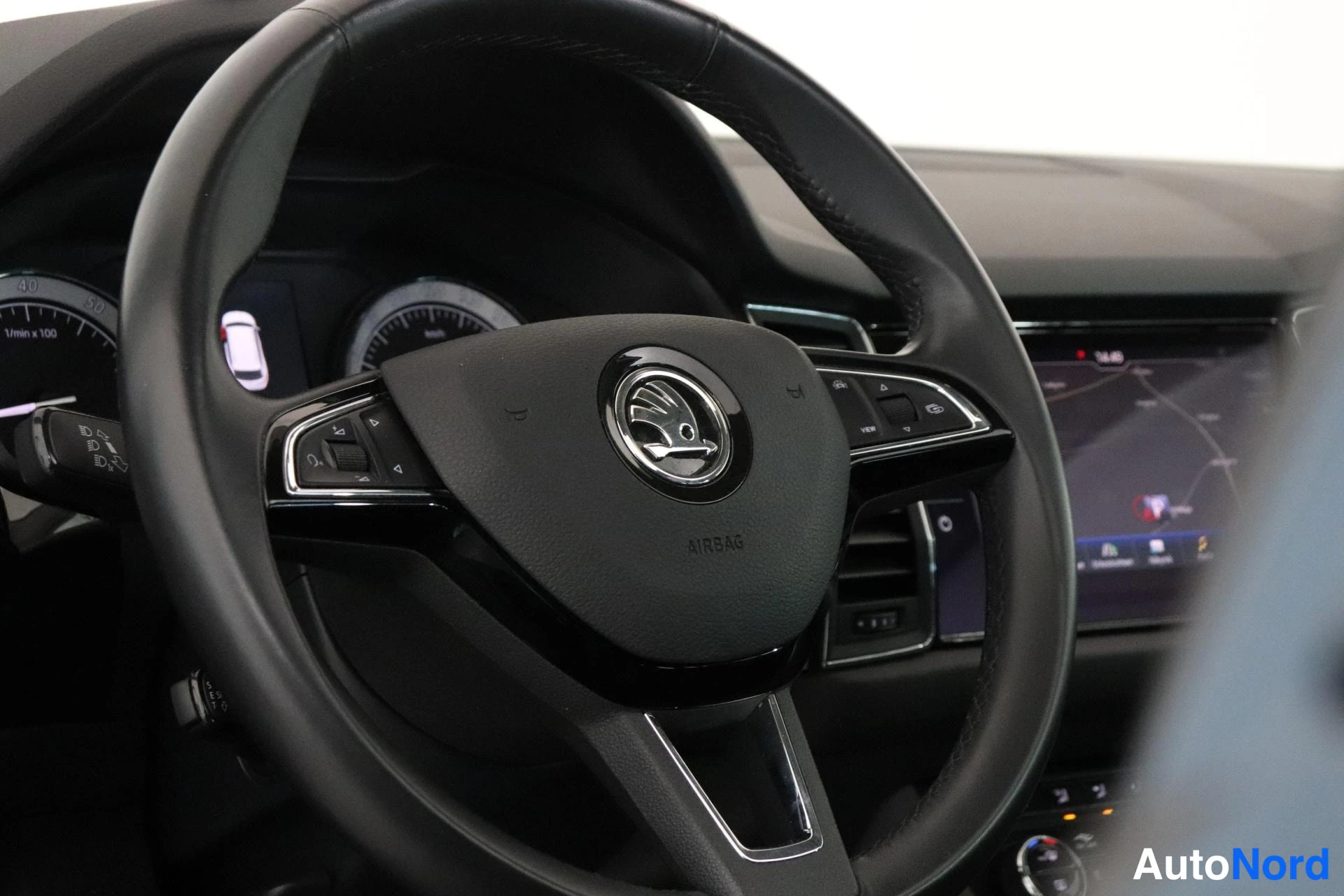 Muu: Lähikuva Škoda-ohjauspyörästä, jossa AIRBAG-teksti ja monitoiminapit; kojelaudan näyttö ja mittaristo osin näkyvissä.