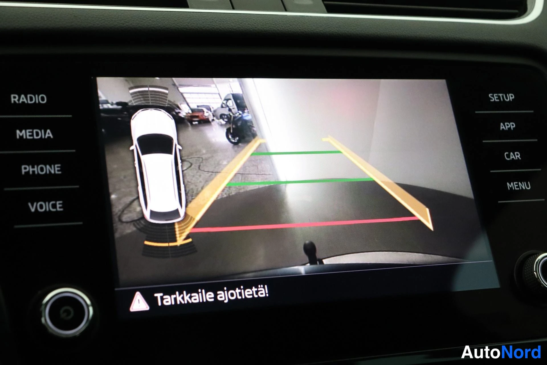 Yksityiskohta: Kosketusnäyttö näyttää peruutuskameran kuvan suuntausviivoilla sekä varoituksella Tarkkaile ajotietä!