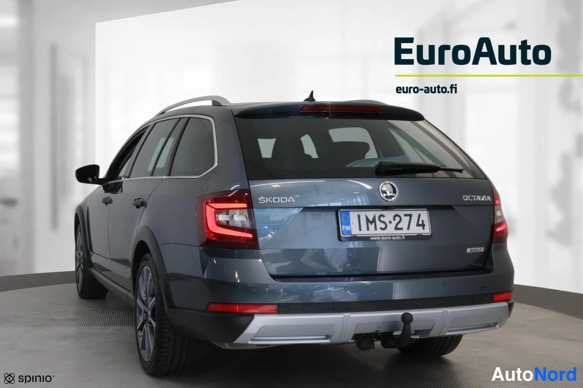 Takaviisto: Sinertävän tummanharmaa Skoda Octavia -farmari takaosta ja vaselta sivulta; perässä ŠKODA- ja OCTAVIA-merkit, rekisteritunnus, kattokaiteet ja hopeinen suoja ta