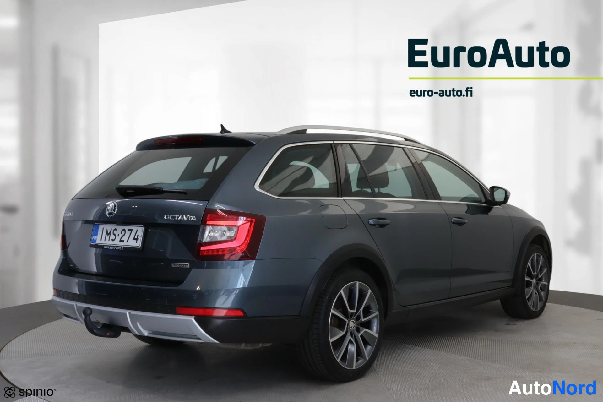 Takaviisto: Sinertävän tummanharmaa Skoda Octavia -farmari takaosta ja vaselta sivulta; OCTAVIA-merkki takaluukussa, rekisteritunnus, hinauskoukku, kattokaiteet ja kevytmet