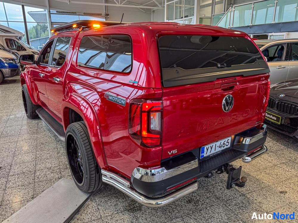 Takaviisto: Punaisen lava-auton takakulma kuvattuna sisätilassa: lavalla lasitettu kate oransseilla merkkivaloilla, takaluukussa VW-merkki ja AMAROK-teksti, V6-tunnus, reki