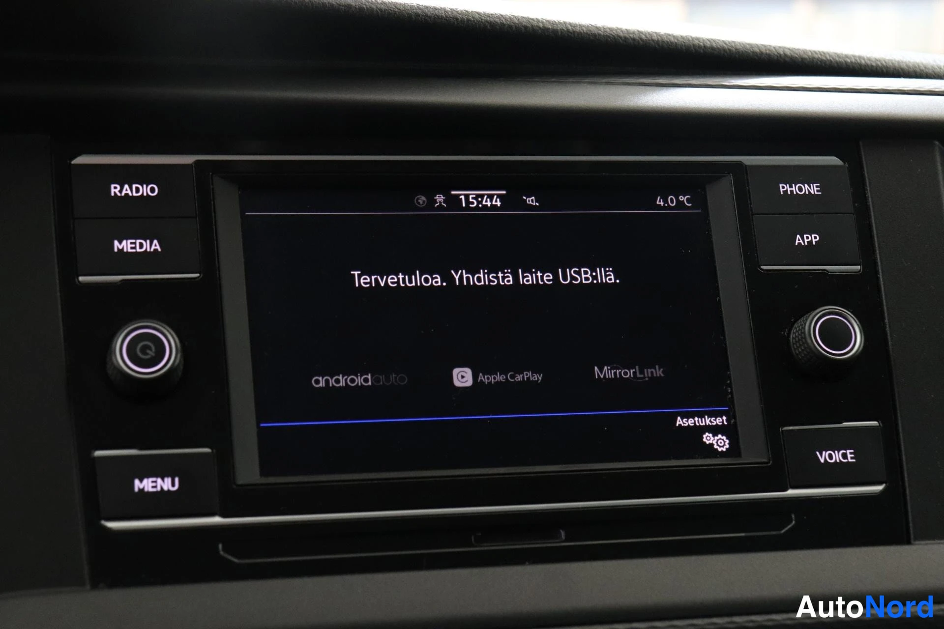 Yksityiskohta: Auton keskikonsolin kosketusnäyttö. Näytöllä teksti 'Tervetuloa. Yhdistä laite USB:llä.' ja alareunassa logot Android Auto, Apple CarPlay ja MirrorLink. Kello 1