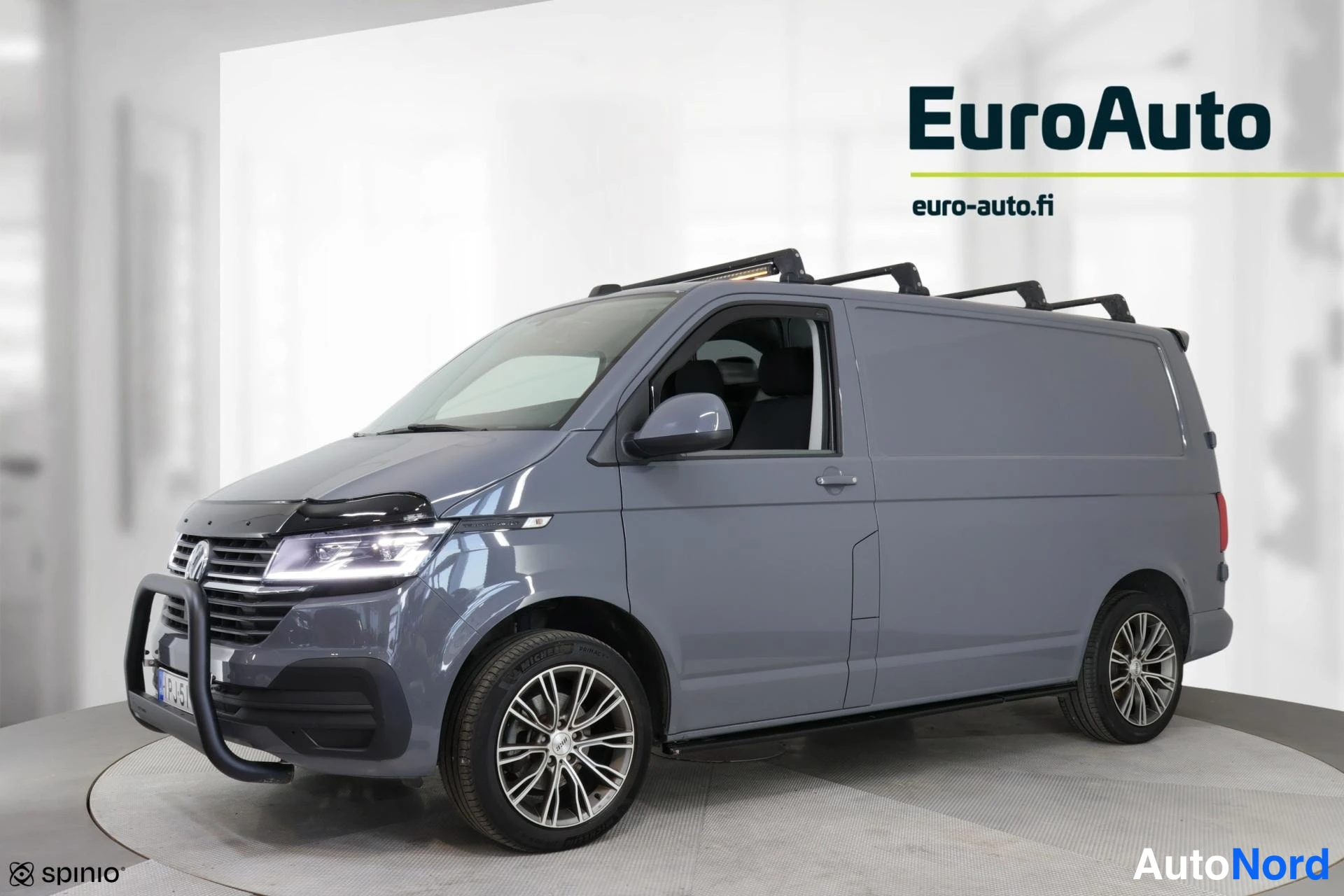 Sivulta: Side view of a closed panel grey van showing roof racks and two-tone alloy wheels. No sliding door handle or window is visible.