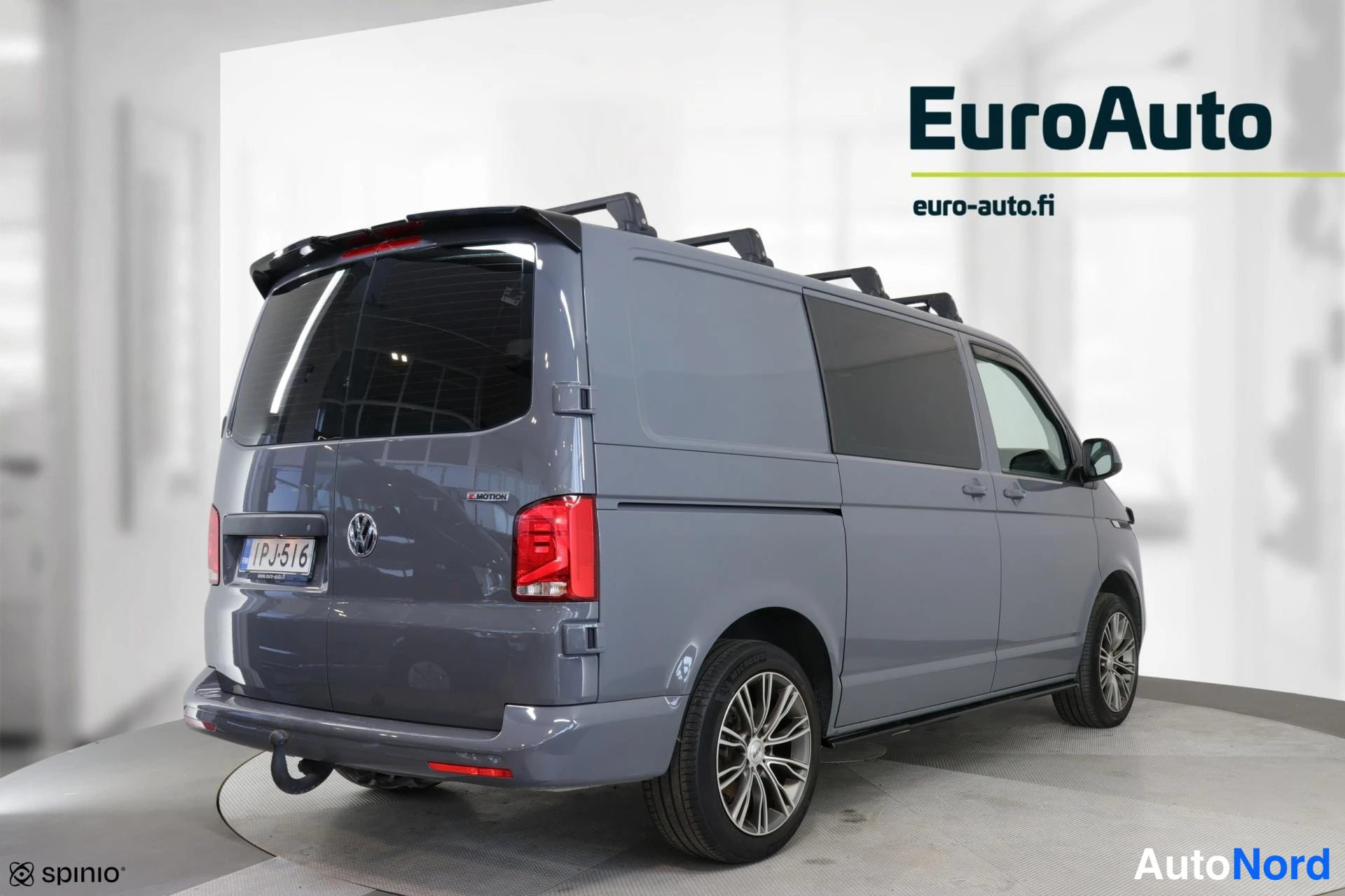 Takaviisto: Rear passenger side three-quarter view of a grey Volkswagen van showing the right flank, sliding door tracks, roof rails, rear taillights, alloy wheels, and a E