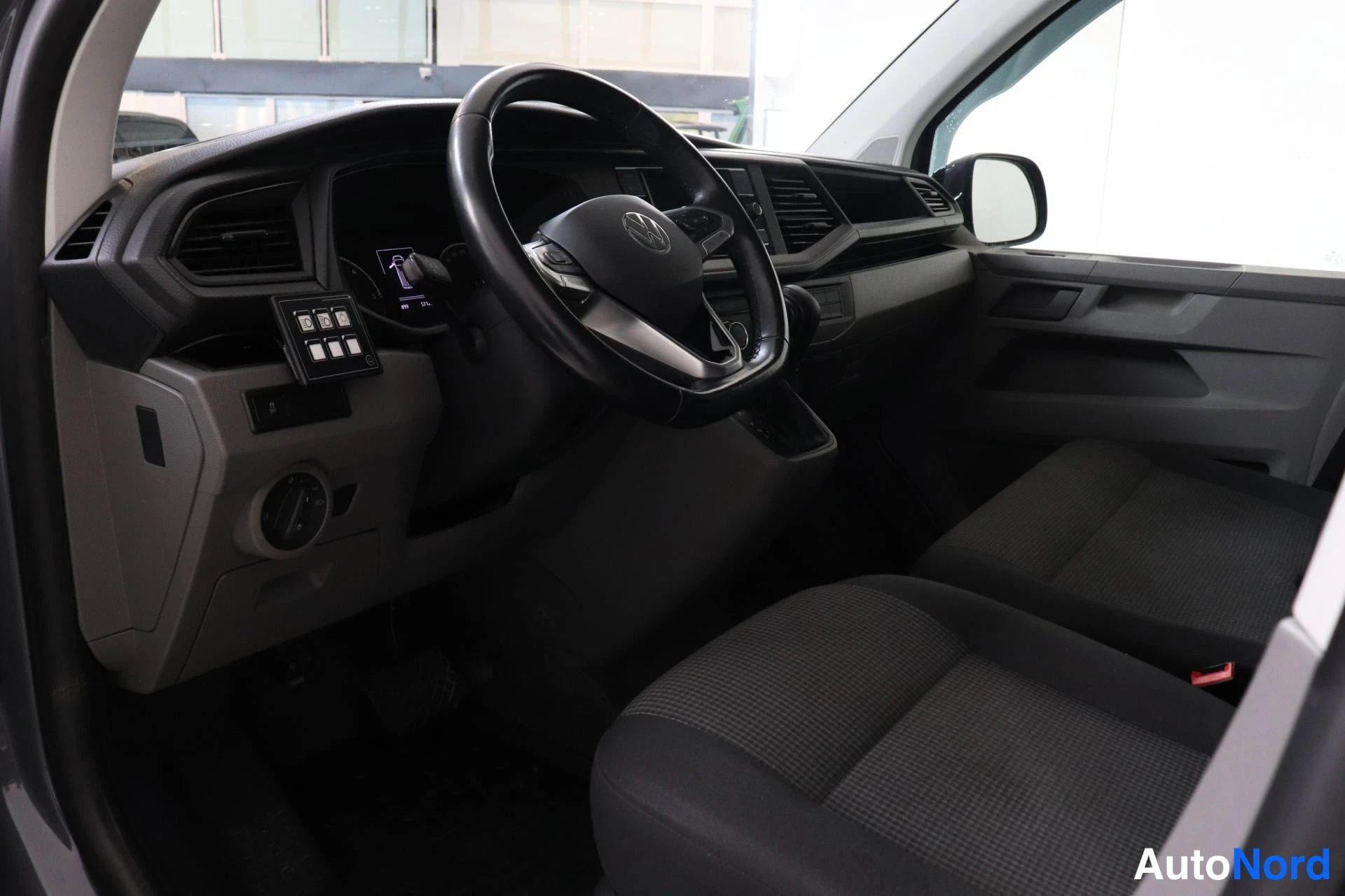 Ohjaamo: Interior view of a vehicle cabin focusing on the driver's seat and dashboard area, showing a black multi-function steering wheel, instrument panel with an illum
