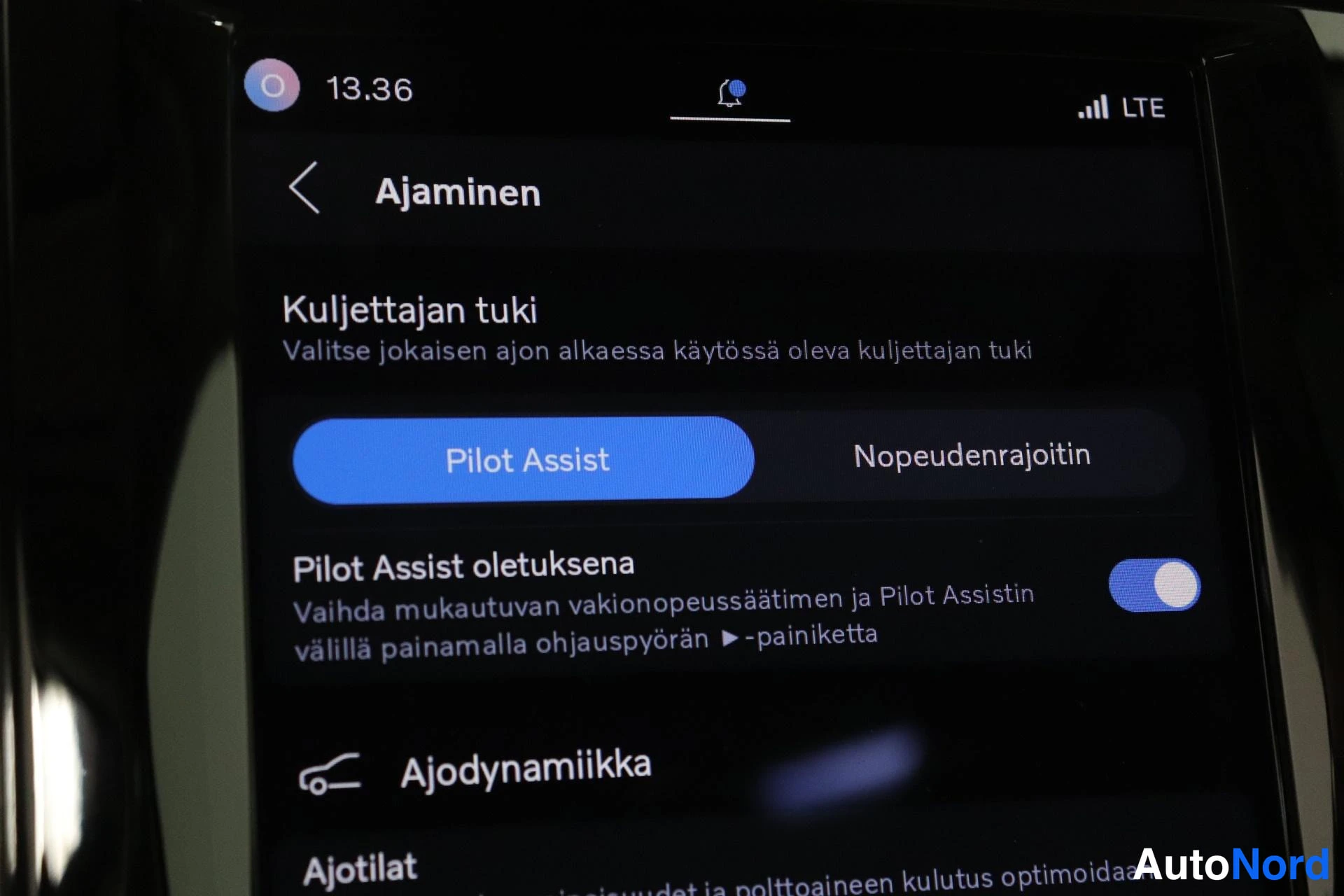 Yksityiskohta: Interior close-up of a digital control display showing 'Ajaminen' (Driving) settings. The driver support section features a blue toggle switch selecting 'Pilot