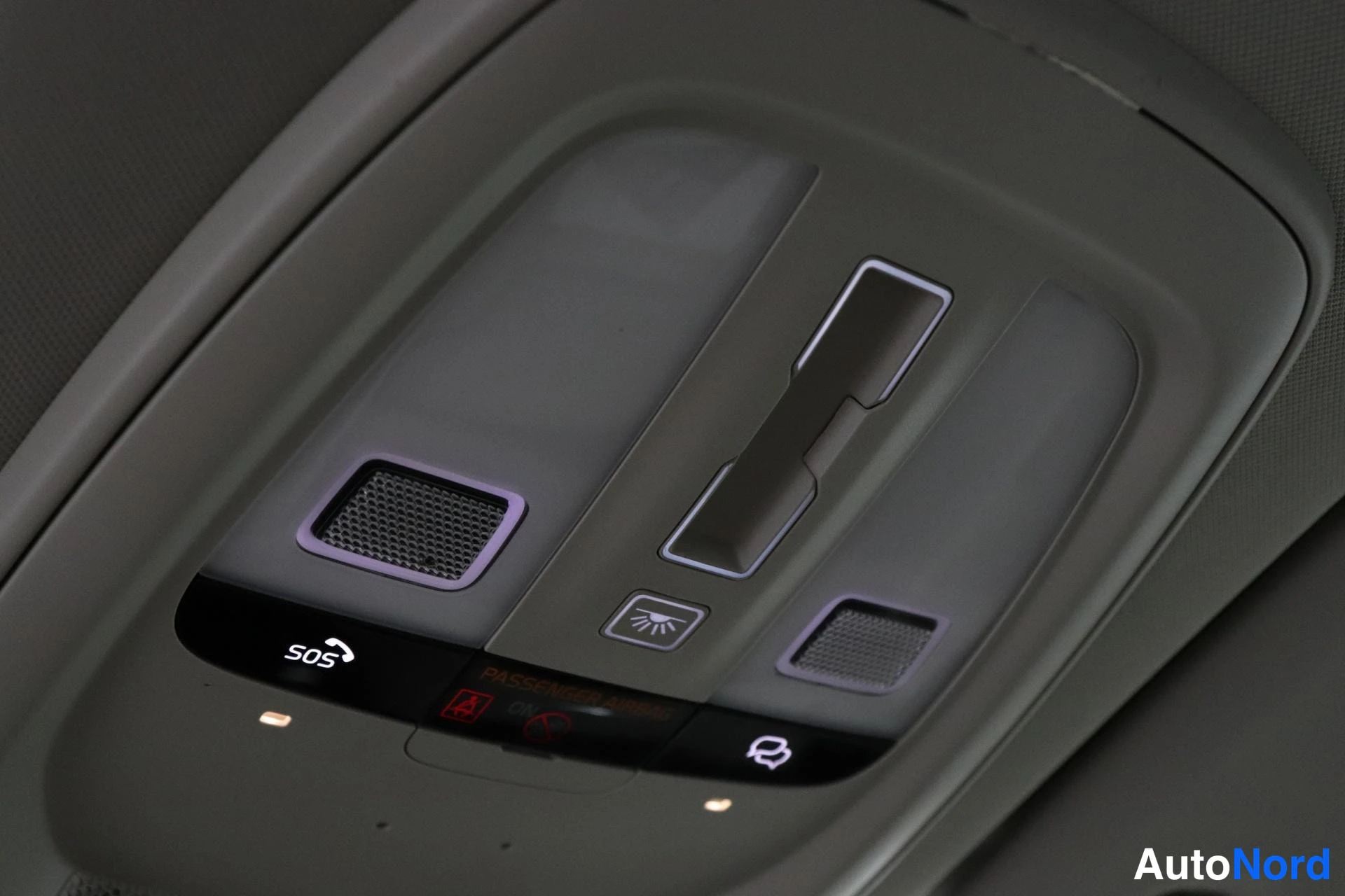 Yksityiskohta: Close-up of the light grey plastic overhead console on the car ceiling. Features include two map lights, illuminated SOS and emergency call buttons, rear lighti