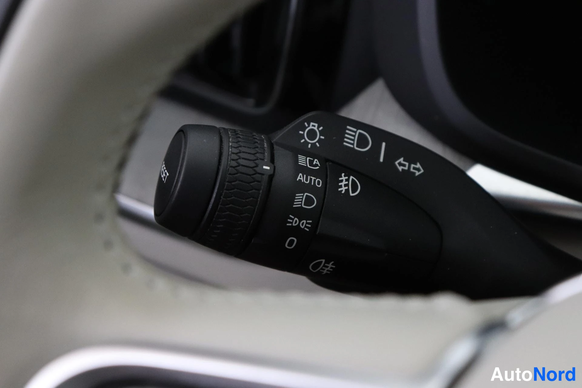 Yksityiskohta: Macro photograph of a black multifunction stalk mounted behind the steering wheel. Visible icons on the stalk indicate functions for headlight auto-on ('AUTO'),