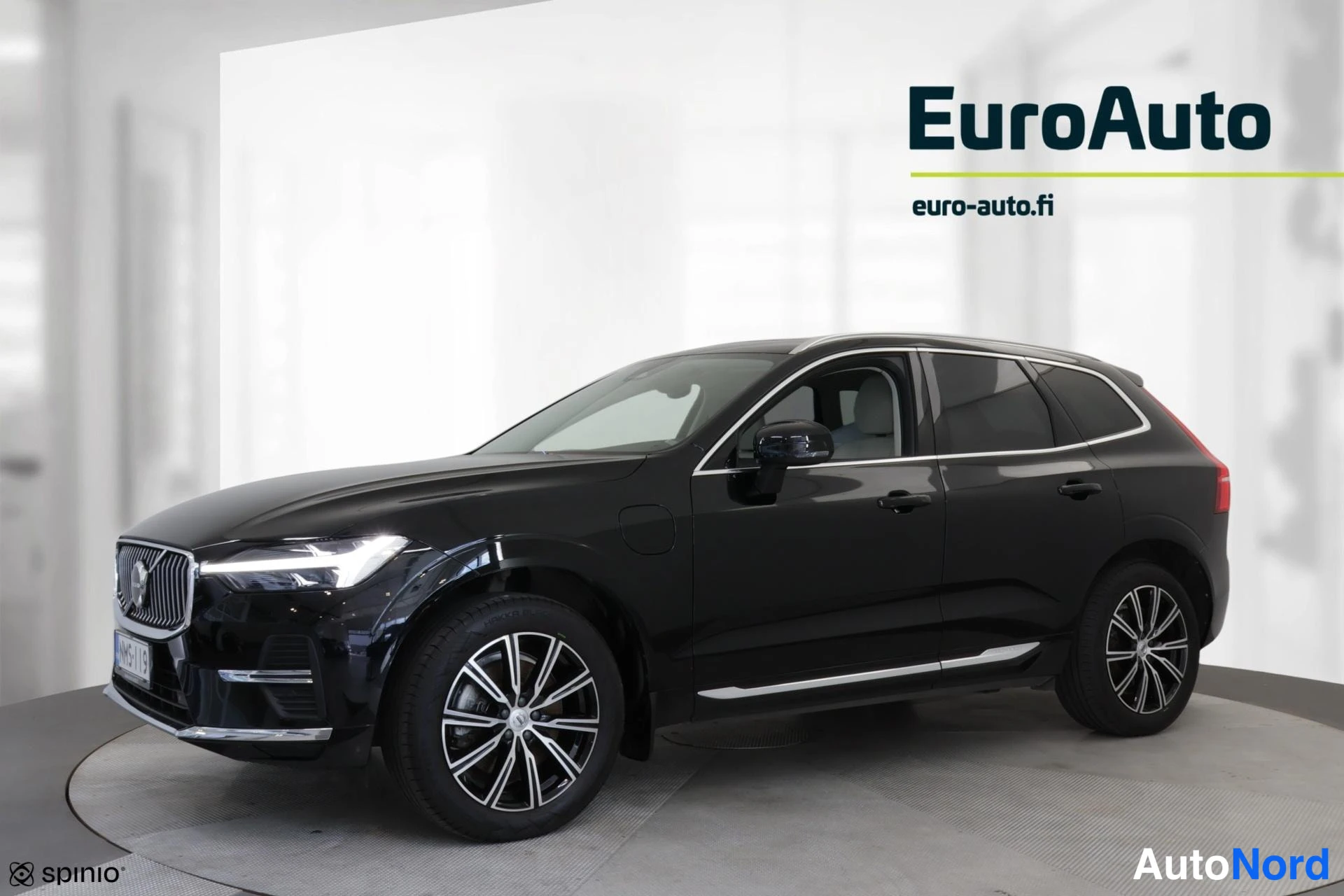 Sivulta: Oikeanpuoleinen sivukuva mustasta VolvoXC60:sta. Kokonaan näkyvä, auto seisoo pyörivällä alustalla studio-tilassa. Valtava rekisterinumero näkyy etuosassa. Vase