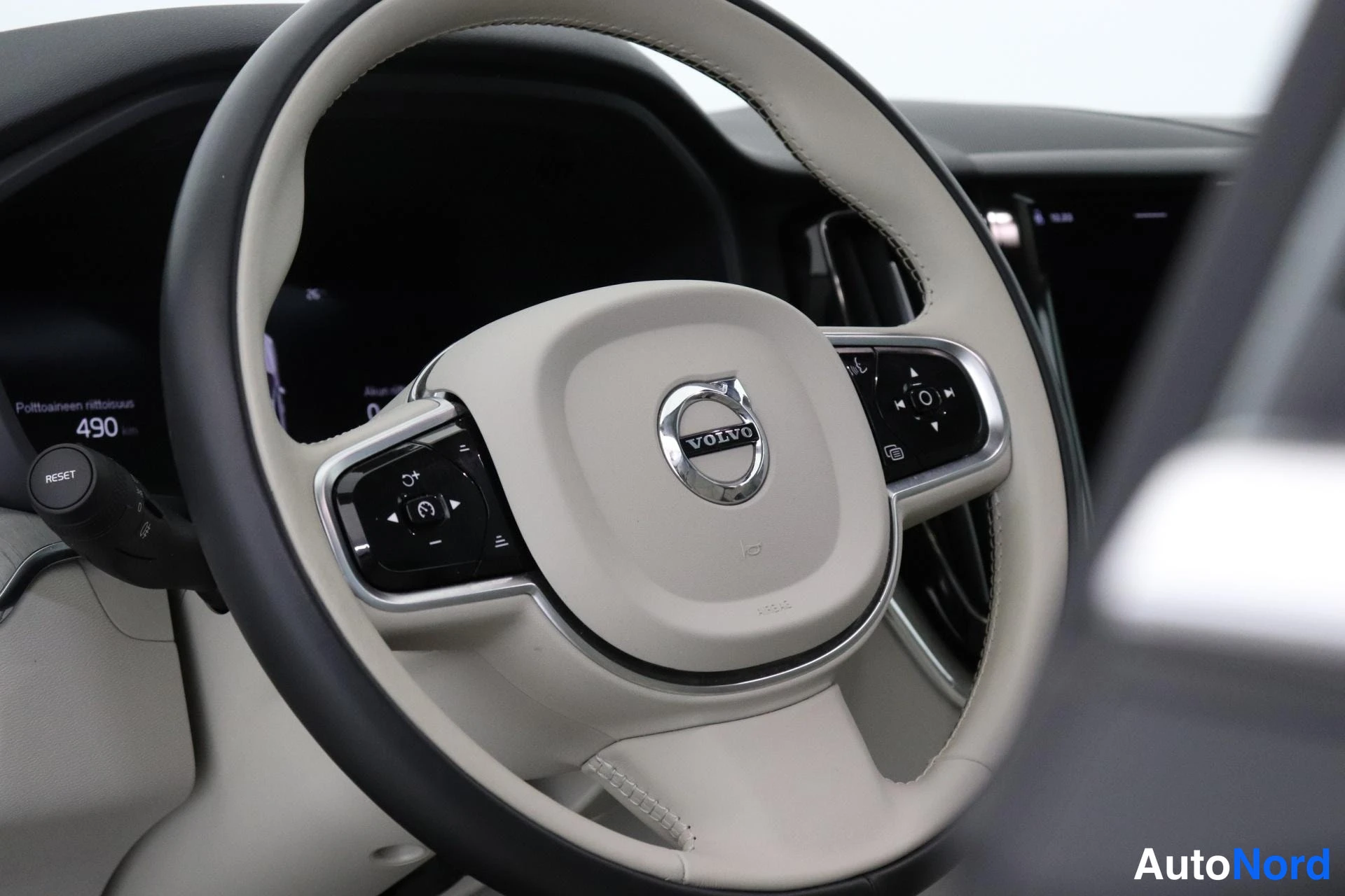 Muu: Volvo-ohjauspyörä beige-meriinipohjaisella kuljettajan puolella, mittaristo näkyy vasemmalla.