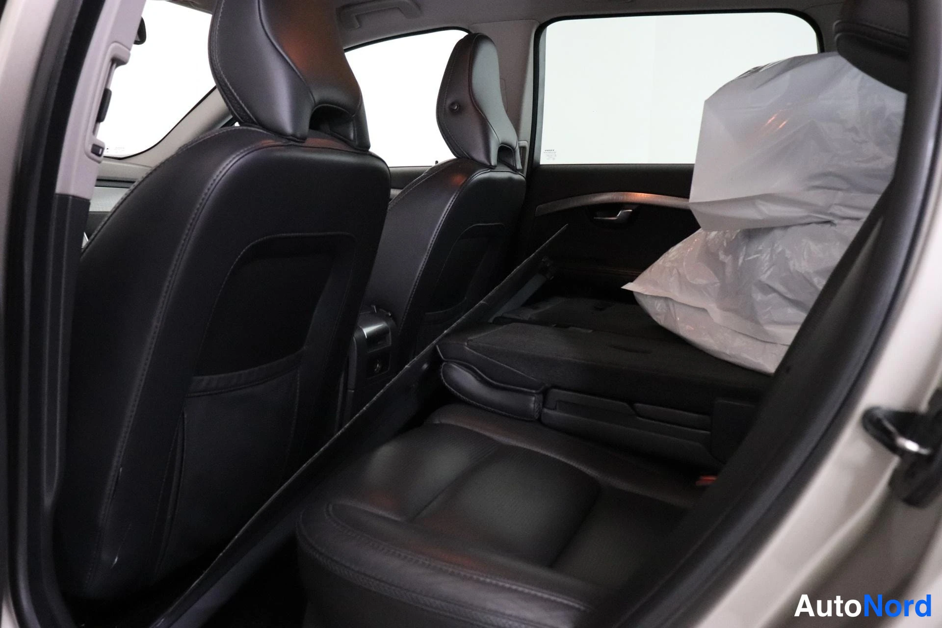 Takaistuimet: The car's rear seats in black leather with headrests. To the right, a folded seat section is wrapped in protective white plastic.