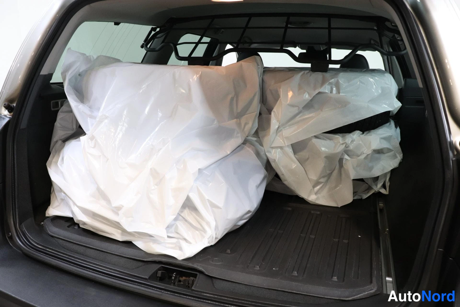 Tavaratila: View into the trunk showing rear seats folded down and covered with large white protective sheets. A cargo net is installed across the roof area.