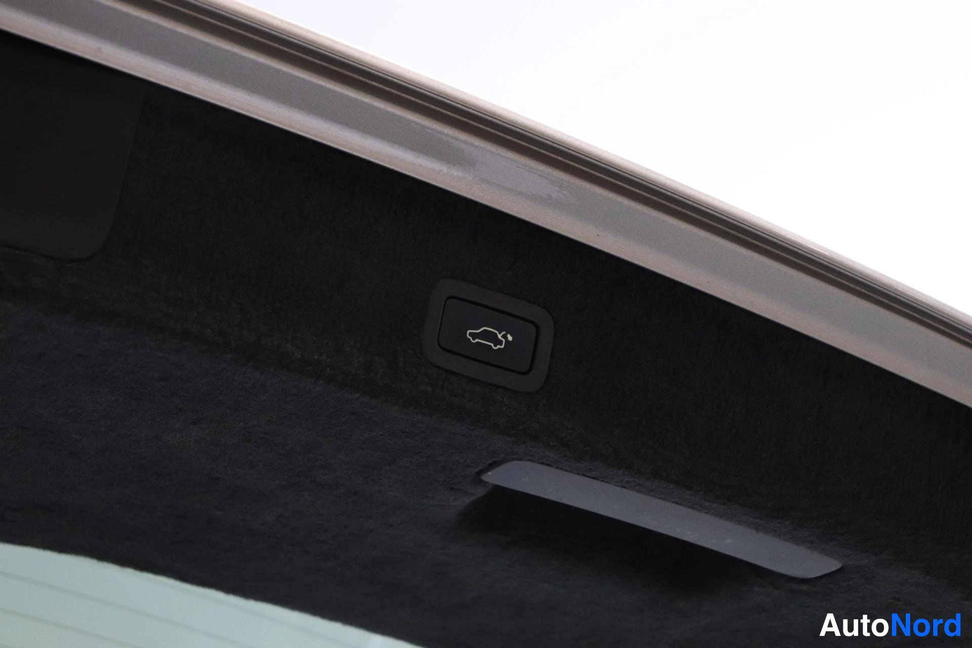 Yksityiskohta: Close-up of a button located inside the trunk with an icon of a hatchback with the lid open, indicating an electric tailgate release.