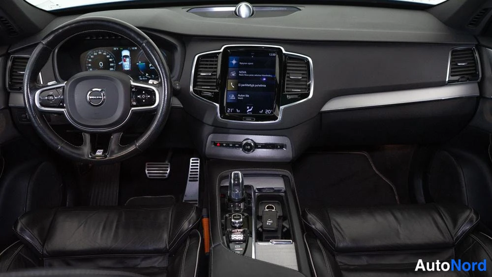 Ohjaamo: Wide view of the front cabin interior showing black leather seats, multifunction steering wheel, digital instrument cluster, center console gear selector, and v