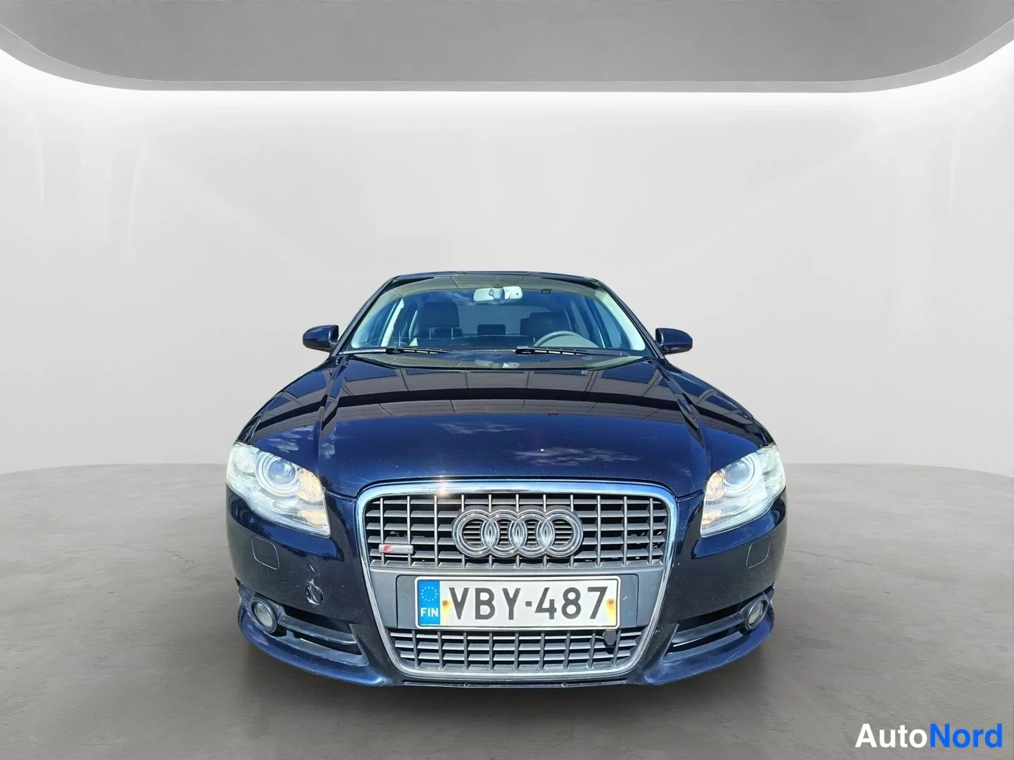 Edestä: Front view of a dark blue Audi sedan showing the grille, headlights, and license plate.