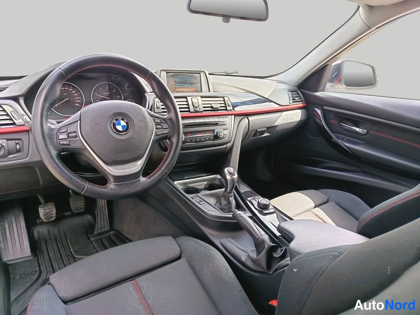 Yksityiskohta: BMW:n ohjaamo: musta sisusta punaisilla korostuksilla, monitoimiohjauspyörä ja keskconsole infotainment-näytöllä.