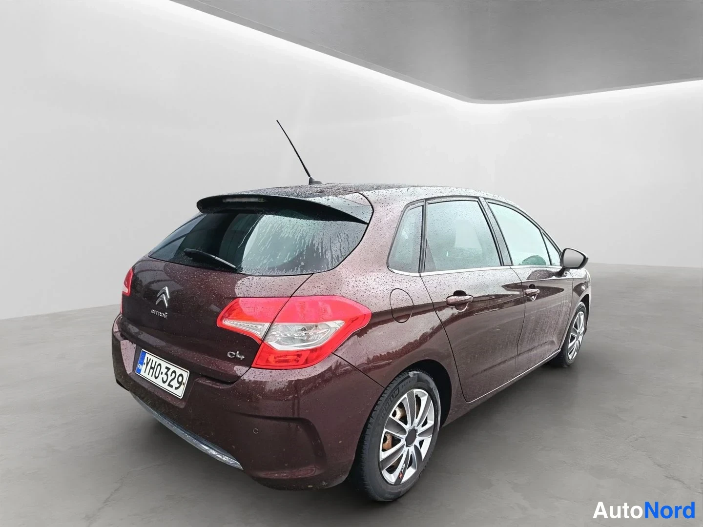 Takaviisto: Tummanpunainen Citroën C4 -viistoperä kuvattu takaviistosta studiotaalustassa; rekisteritunnus YH0-329, takaovi ja osa etuovesta näkyvissä.