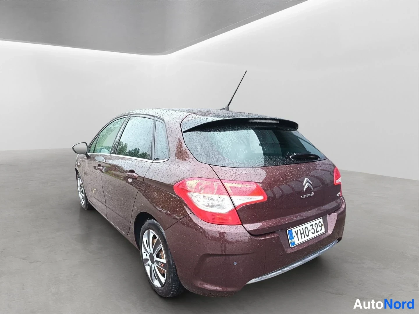 Takaviisto: Tummanpunainen Citroën C4 kuvattu takaviistosta vasemmalta; rekisteritunnus YH0-329 ja Citroën-merkki takaluukussa näkyvissä.