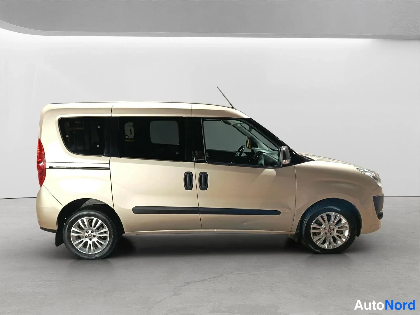 Sivulta: Fiat Doblo sivulta vasemmalta, vaalean beige korit, mustat ovenkahvat ja sivulistit, pikkutarkka studiovaalea tausta.