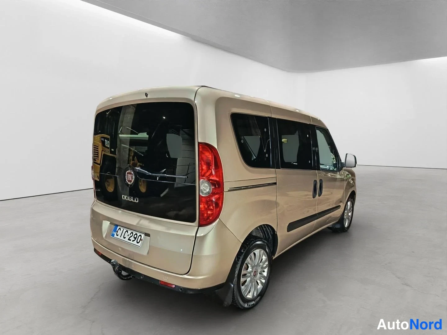 Takaviisto: Back left three-quarter view of a beige van with the Fiat logo and model name 'DOBLO' visible on the rear glass, along with an EU license plate reading ''.