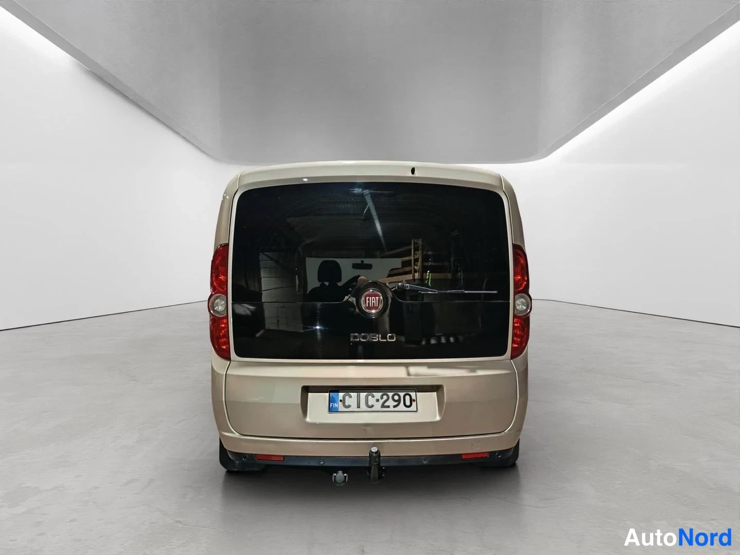 Takaa: Direct rear view of a beige Fiat Doblo van showing vertical tail lights, the Fiat emblem, the model name 'DOBLO', a Finnish license plate reading '', and a tow