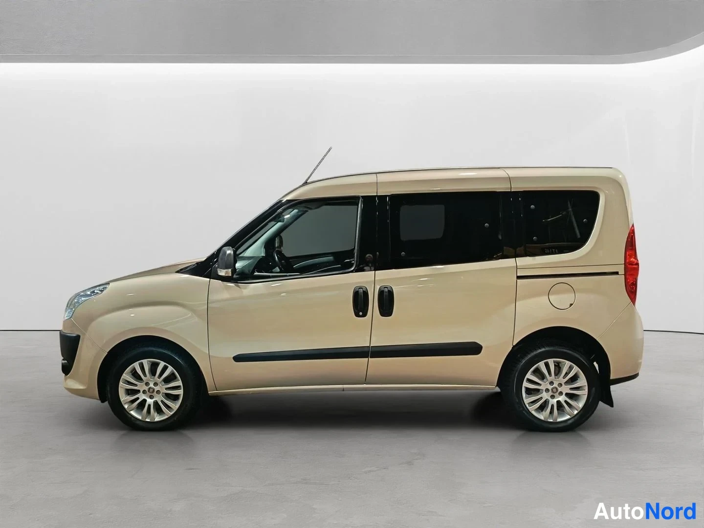 Sivulta: Side profile view of a beige van standing against a white background, showcasing the front and rear wheels, sliding door handle, and side mirrors.