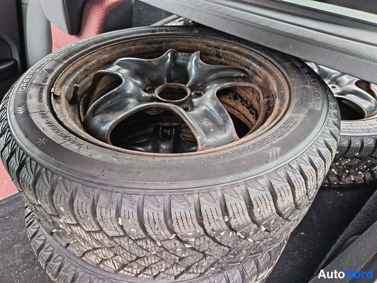 Yksityiskohta: Takaluukissa pinottuna neljä napatyreellä varustettua talvirengasta mustilla teräsvanteilla; renkaiden sivussa tekstit Nokia Snowproof ja Goodyear.