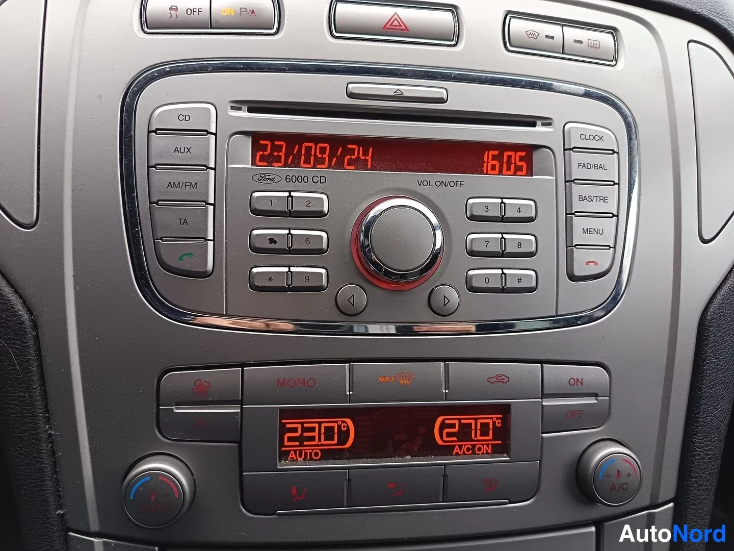 Muu: Kojelaudan keskikonsolin lähikuva: Ford 6000 CD -radiolaite näytöllä 23/09/24 ja kello 16:05, CD-, AUX-, AM/FM- ja TA-painikkeet sekä kaksivyöhykeilmastointi nä